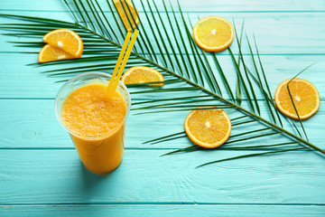 Plastic cup of tasty orange smoothie on color wooden table