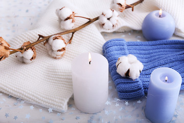 Knitted hat, candles and cotton flowers on light background
