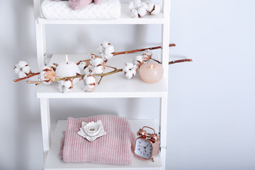 Warm clothes, cotton flowers and candles on shelves near light wall