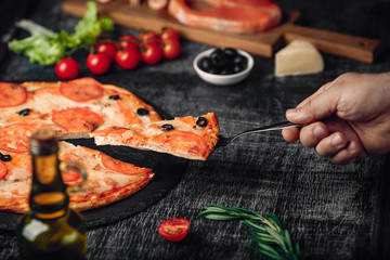 Sliced slice of pizza in hand with cheese, trout, tomatoes cherry, olives and shrimps on chalk board.