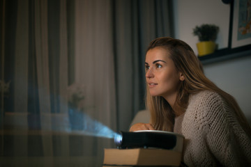 Woman on sofa watching movie using digital LCD video projector, home theater
