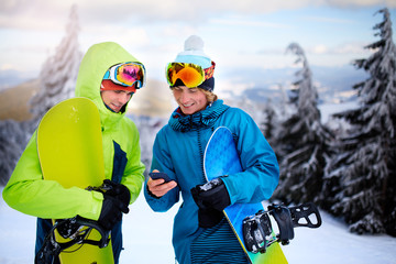 Two snowboarders talking and holding smartphones. Friends looking at cellphone and communicating in...