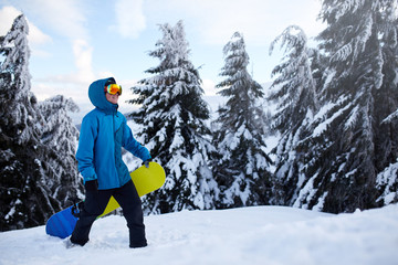 Snowboarder climbing to mountain top carrying his snowboard through forest for backcountry freeride...