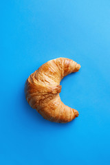 Single fresh croissant isolated on a blue background viewed from above. Top view