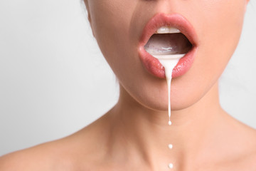 Fototapeta Young woman with white liquid dripping from her mouth on light background. Erotic concept obraz