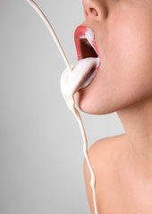 Fototapeta White liquid dripping into woman's mouth on light background. Erotic concept obraz