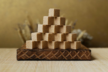 Cubes of brown sugar on the kitchen table. Rustic still life with wooden and glass utensils.
