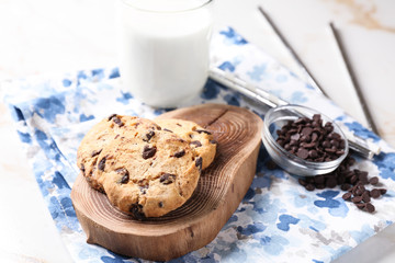 Tasty cookies, bowl with chocolate chips and glass of milk on table
