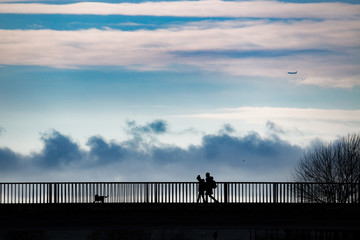 People in silhouette standing on a bridge over a sea