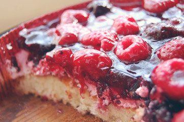 Slice of delicious tasty blueberry pie with jelly top with cream and bright pink rapsberries on it at cardboard background.