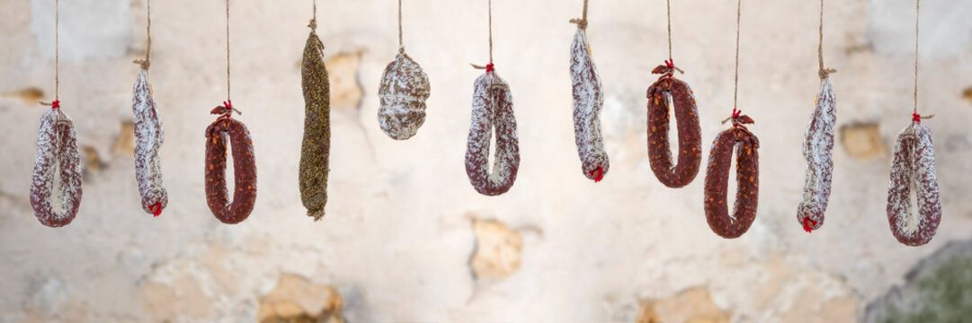 Panoramic Selection of French dry charcuterie hanging over old brown white cracked wall background.