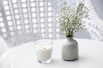 Burning candle and vase with flowers on table