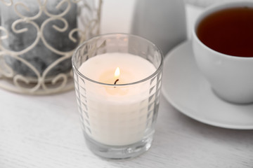 Burning candle and cup of tea on white wooden table
