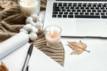 Laptop, open notebook and burning candles on white wooden table