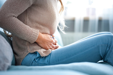 Young woman suffering from abdominal pain while sitting on sofa at home