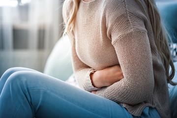 Young woman suffering from abdominal pain while sitting on sofa at home