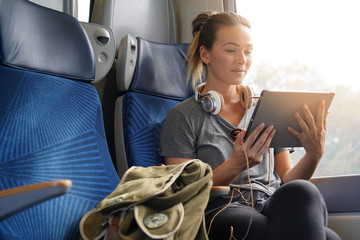 Young woman travelling by train with tablet and headphones - obrazy, fototapety, plakaty