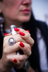 Caucasian woman with red nails manicure and antique ring on finger holds small vape. Smoking alternative vay. Life without cigarettes. Woman-vaper. Small e-cigarette.