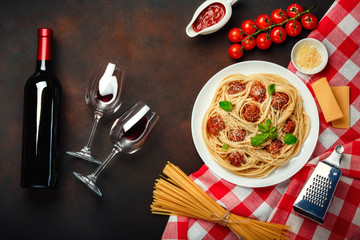 Spaghetti pasta with meatballs, cherry tomato sauce, cheese, wineglass and bottle on rusty...