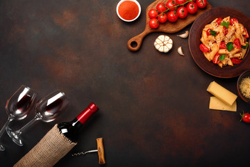 Pasta with cheese, cherry tomato sauce, wineglass and bottle wine, corkscrew, garlic, turmeric on rusty background.