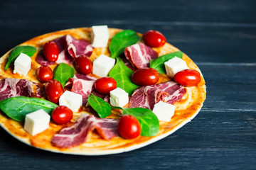 pizza with ham, whole tomatoes and cheese, basil on wooden background