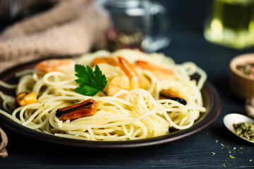 spaghetti with seafood in a plate and spices on a wooden board