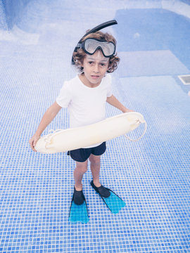 Boy in diving equipment with lifebuoy in empty pool
