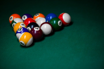 Sport billiard balls set arranged in shape of triangle on green billiard table in pub. Players are ready for the first hit of the round to start the billiard game.