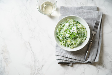 Spinach risotto with a glass of white wine on marble background with copy space