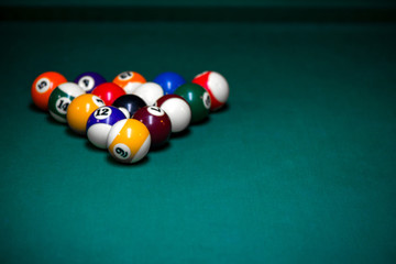 Sport billiard balls set arranged in shape of triangle on green billiard table in pub. Players are ready for the first hit of the round to start the billiard game.