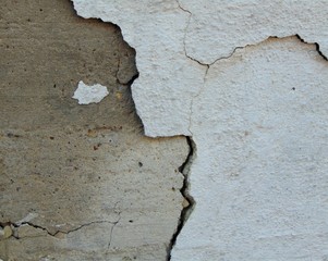 large crack in the center of the wall. half the wall is white and half is gray concrete.