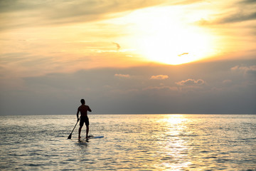 Sunset Silhouette Of Young Handsome Man Paddling On Surfboard Toward The Horizon In The Open Sea Beautiful Scenic Sunset