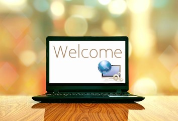 Black laptop with welcome text and computer graphic design in white screen on wooden table floor...