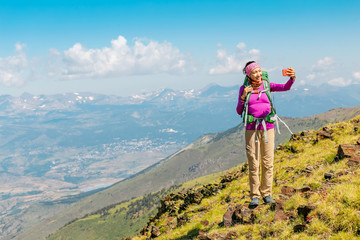 Fototapeta premium woman hiker taking photo with her smart phone on the top of the mountain peak