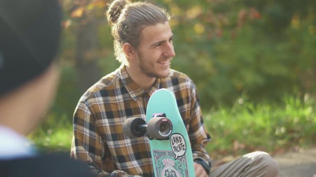 Smiling guy in a plaid shirt customizing a skateboard. Young man with a skateboard outdoors.
