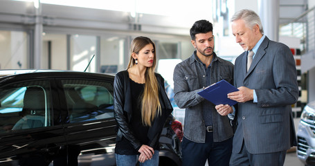 Obraz premium Car dealer exaplining a car's features to a couple by reading a document