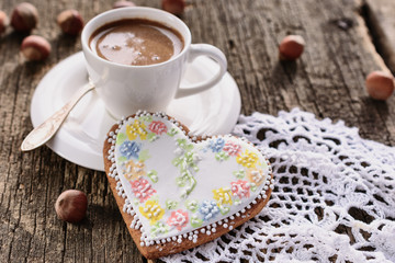 A white cup of freshly brewed coffee on a white saucer and a beautiful heart-shaped gingerbread on...