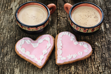 Two full cups of coffee next to two heart-shaped gingerbreads are close to each other