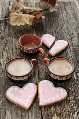 Two full cups of coffee next to two heart-shaped gingerbreads are close to each other and one empty coffee cup next to a broken heart-shaped gingerbread at a distance on old wooden boards, vertical 