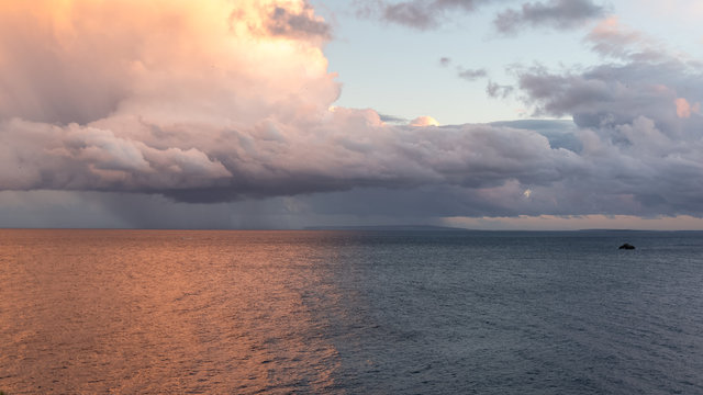 Panorama of the ocean, mediterranean sea, in the evening, sunset with the rain in background, a rock alone in the sea

