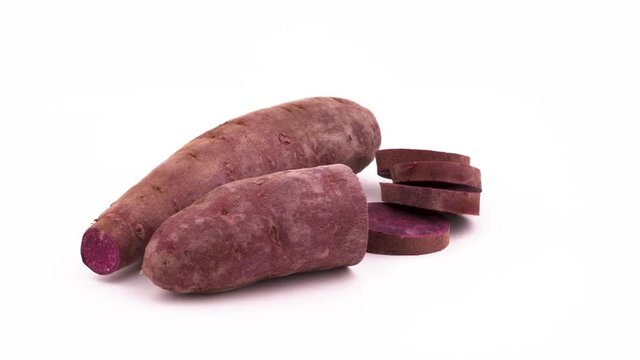 One whole, one half sweet potato and few purple batata slices rotating on the turntable. Isolated on the white background. Close-up. Macro.