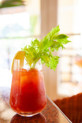 Delicious and classic Bloody Mary cocktail or tomato juice garnished with celery stalk and lemon wedge on a table by the window. Good for hangover. Bright and healthy theme. Natural morning light.