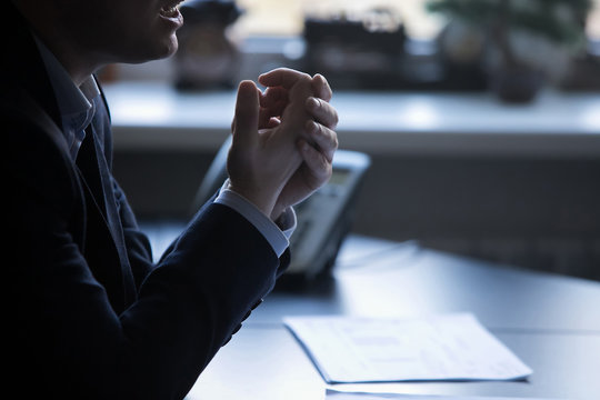 A man in a dark suit gesticulates with his hands during a speech. Open palms