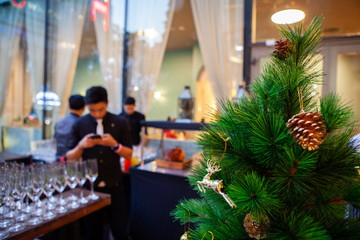 Small green Christmas tree with pine cones, sparkling gold and red ball ornaments and decoration. Happy New Year festive celebration. Season Greeting. Window display city background. Natural light.
