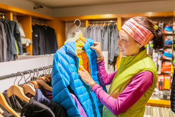 Portrait of a cheerful young woman choosing items in the sport outdoor hiking store clothes shop