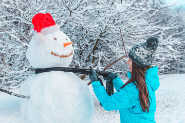 woman make a snowman in frosty winter day