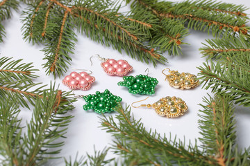 Women's earrings and beaded bracelet among the branches of spruce. On a white background.