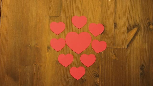 The girl lays out on the wooden table hearts for valentines from red cardboard. Time laps