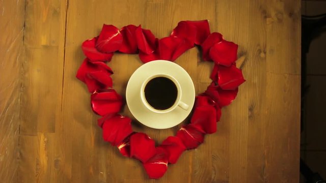 The girl puts in the middle of the heart of rose petals a cup of coffee