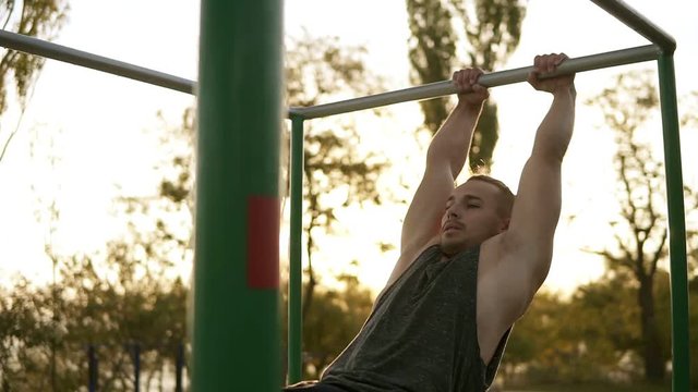 Handsome man having calisthenics training on horizontal bar outdoors. Does gymnastic stunts on the crossbar in the park